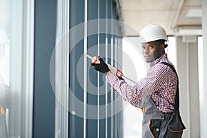 African Workman in overalls installing or adjusting plastic windows in the living room at home