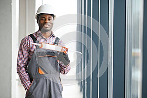 African Workman in overalls installing or adjusting plastic windows in the living room at home