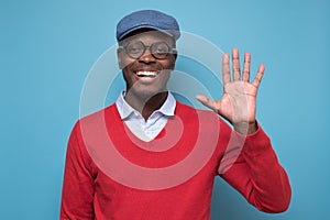 African young man with blue hat saying hello, waving a hand