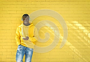 African Young Man Listening Music Leaning On Yellow Wall