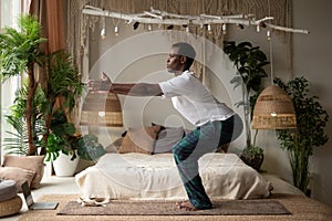 African young man practicing yoga indoors in a retreat space doing Chair pose or Utkatasana