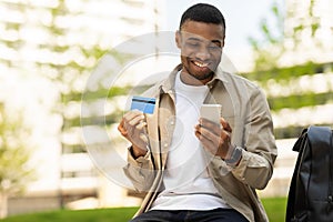 African young man shopping online with credit card using smartphone outdoors