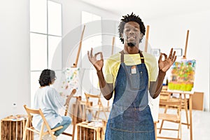 African young man standing at art studio relax and smiling with eyes closed doing meditation gesture with fingers