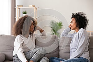 African young mom listening teen daughter sitting on couch together