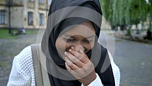 African young muslim woman in hijab laughing in camera and standing in park near university, happy and cheerful