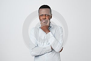 African young thinking man looks up with hand near face isolated on white background.