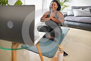 African young woman doing yoga virtual fitness class with laptop at home