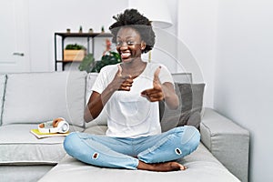 African young woman sitting on the sofa at home pointing fingers to camera with happy and funny face