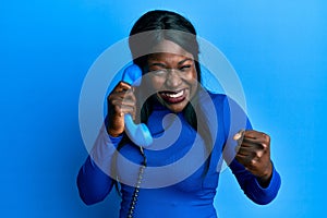 African young woman speaking on vintage telephone screaming proud, celebrating victory and success very excited with raised arms