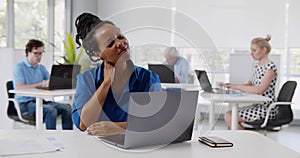 African young woman suffering with pain massaging neck while working in office