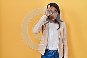 African young woman wearing glasses doing ok gesture shocked with surprised face, eye looking through fingers