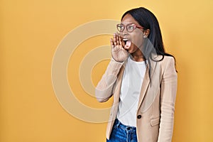 African young woman wearing glasses shouting and screaming loud to side with hand on mouth