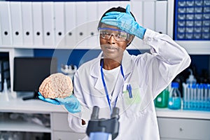 African young woman working at scientist laboratory holding brain stressed and frustrated with hand on head, surprised and angry