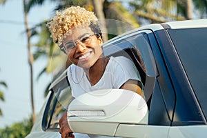 Afro american blonde curly hair girl with beautiful bright teeth sitting in her car at tropical journey