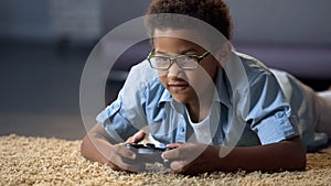 Afro-American boy absorbedly playing on new video game console, home activity