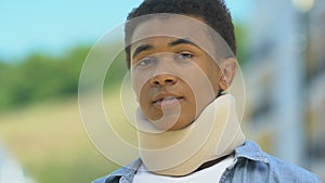 Afro-american boy in foam cervical collar looking upset outdoors, neck injuries
