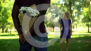 Afro-american boyfriend hiding flowers bouquet behind back in park, surprise