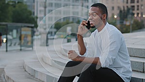 Afro american business man african student ethnic black guy sitting on steps in city outdoors talking speaking on phone