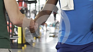 Afro-american and caucasian friends shaking hands in gym after active workout