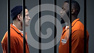 Afro-american and caucasian inmates looking at each other in cell, conflict