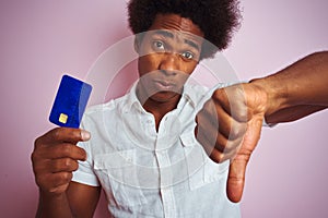 Afro american customer man holding credit card standing over isolated pink background with angry face, negative sign showing