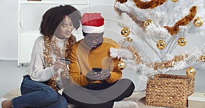 Afro american family couple man and woman make purchase online using smartphone and credit card, buy New Year gifts on