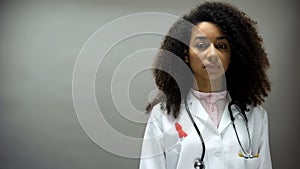 Afro-American female doctor with red ribbon, international AIDS awareness sign