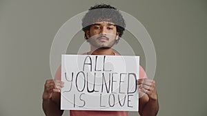 An Afro American guy activist pacifist with a direct confident gaze shows poster with the slogan for love, peace, unity