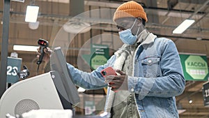 Afro- American guy types on smartphone at grey self-checkout