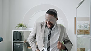 Afro-American guy using laptop then dancing and doing high-five with coworkers in office