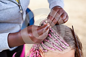 Afro American hairdresser hands made pink dreadlocks in African style for young European girl