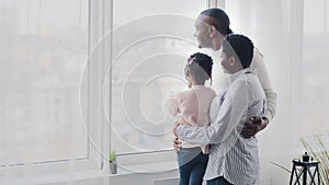 Afro american happy family, black parents young mother and adult father hugging little daughter baby child looking out