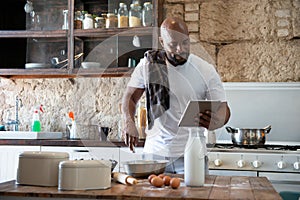 Afro-american man cooking while looking at the recipe online on his tablet
