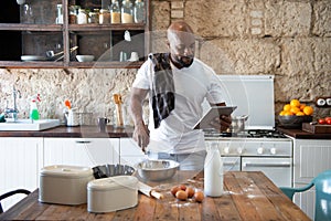 Afro-american man cooking while looking at the recipe online on his tablet