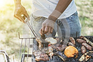 Afro american man cooking meat on barbecue - Chef putting some sausages on grill in park outdoor - Concept of eating outdoor