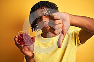 Afro american man with dreadlocks holding red currants over  yellow background with angry face, negative sign showing