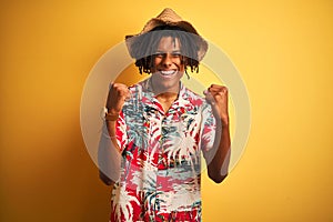 Afro american man with dreadlocks wearing floral shirt and hat over isolated yellow background celebrating surprised and amazed