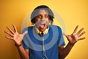 Afro american man with dreadlocks wearing headphones over isolated yellow background celebrating crazy and amazed for success with
