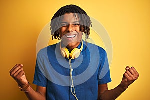 Afro american man with dreadlocks wearing headphones over isolated yellow background celebrating surprised and amazed for success