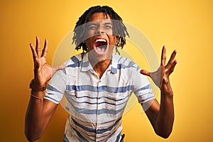 Afro american man with dreadlocks wearing striped shirt over isolated yellow background celebrating mad and crazy for success with