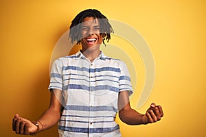Afro american man with dreadlocks wearing striped shirt over isolated yellow background celebrating surprised and amazed for