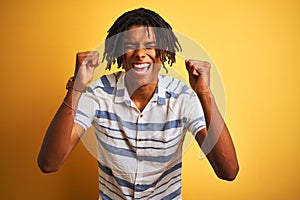 Afro american man with dreadlocks wearing striped shirt over isolated yellow background excited for success with arms raised and