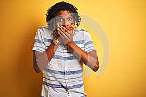 Afro american man with dreadlocks wearing striped shirt over isolated yellow background shocked covering mouth with hands for