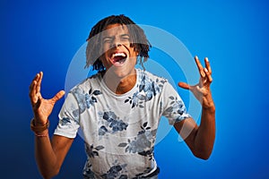 Afro american man with dreadlocks wearing summer floral t-shirt over isolated blue background celebrating mad and crazy for