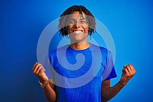 Afro american man with dreadlocks wearing t-shirt standing over isolated blue background celebrating surprised and amazed for