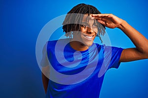 Afro american man with dreadlocks wearing t-shirt standing over isolated blue background very happy and smiling looking far away