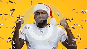Afro-American man in santa hat dancing under falling confetti, carnival party