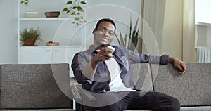 Afro american mixed race guy black male student relaxing at home living room couch watching tv online video movies
