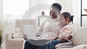 Afro american mother mom woman and little black African girl daughter child kid sitting at home using laptop computer