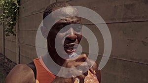 Afro American professional runner man sweating thirsty drinking water holding bottle cooling off after hard urban running workout